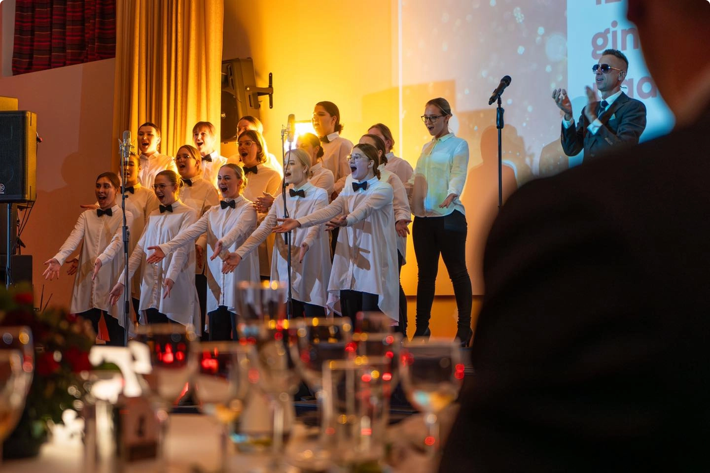 Dainuojantys ir rankas ištiesę choristai su Linu Adomaičiu jaukiame pasirodyme